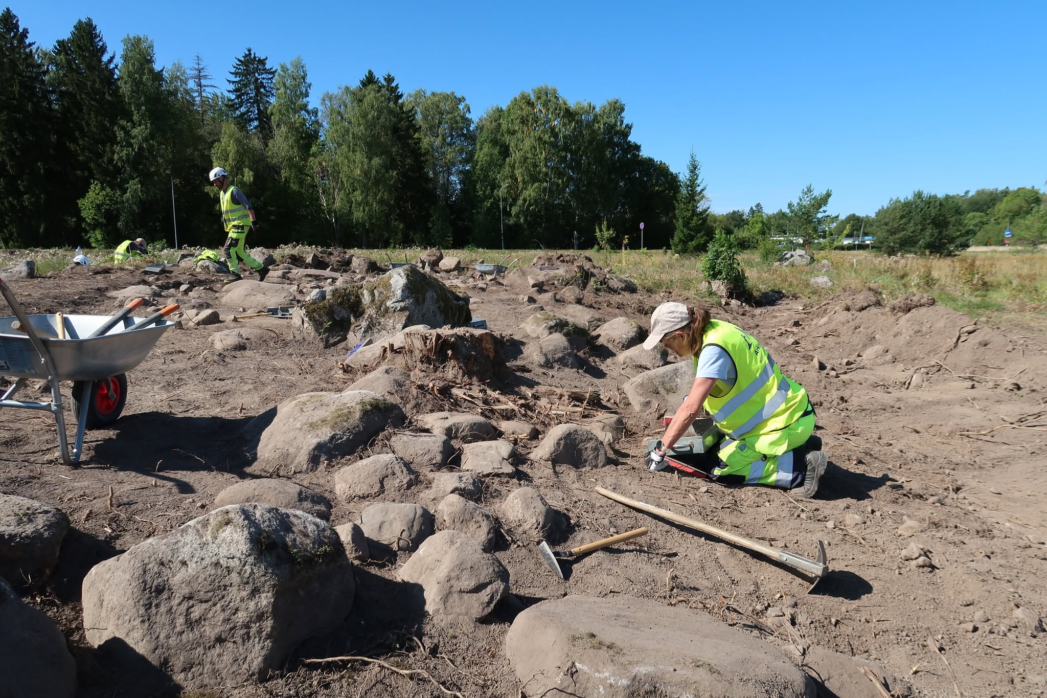Utgrävningsplats med två personer som arbetar framför en skog.