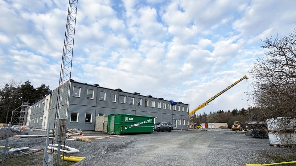 Byggnation av en modulskola på en grusyta med gul lyftkran i bakgrunden.