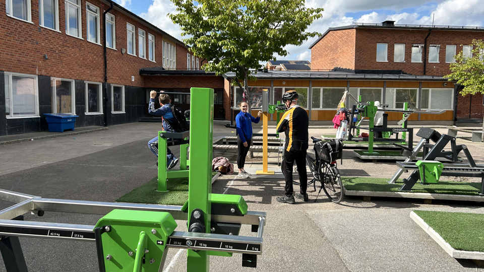 Skolgård med utegym där barn och äldre tränar.
