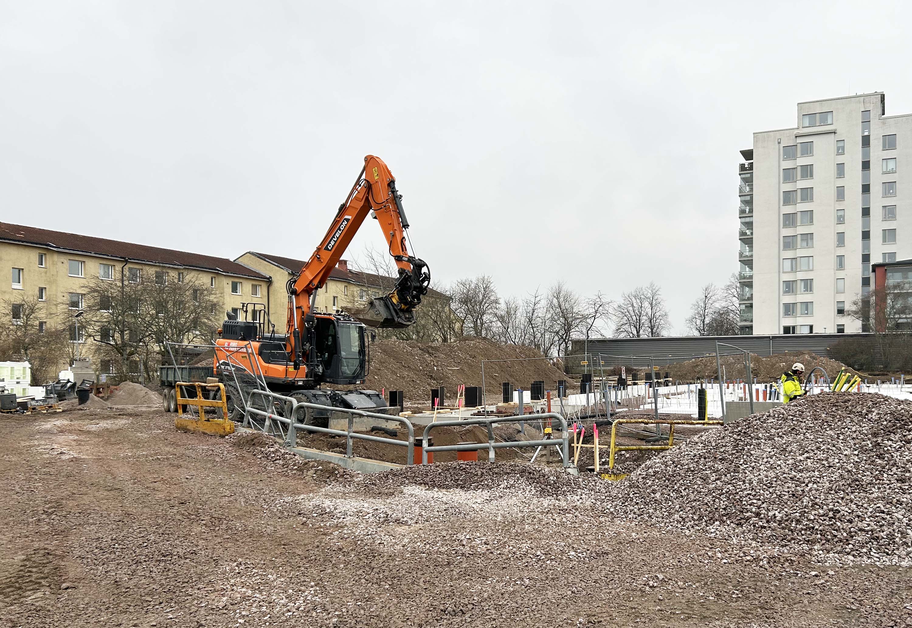 Orange grävmaskin gräver jord på en byggplats.