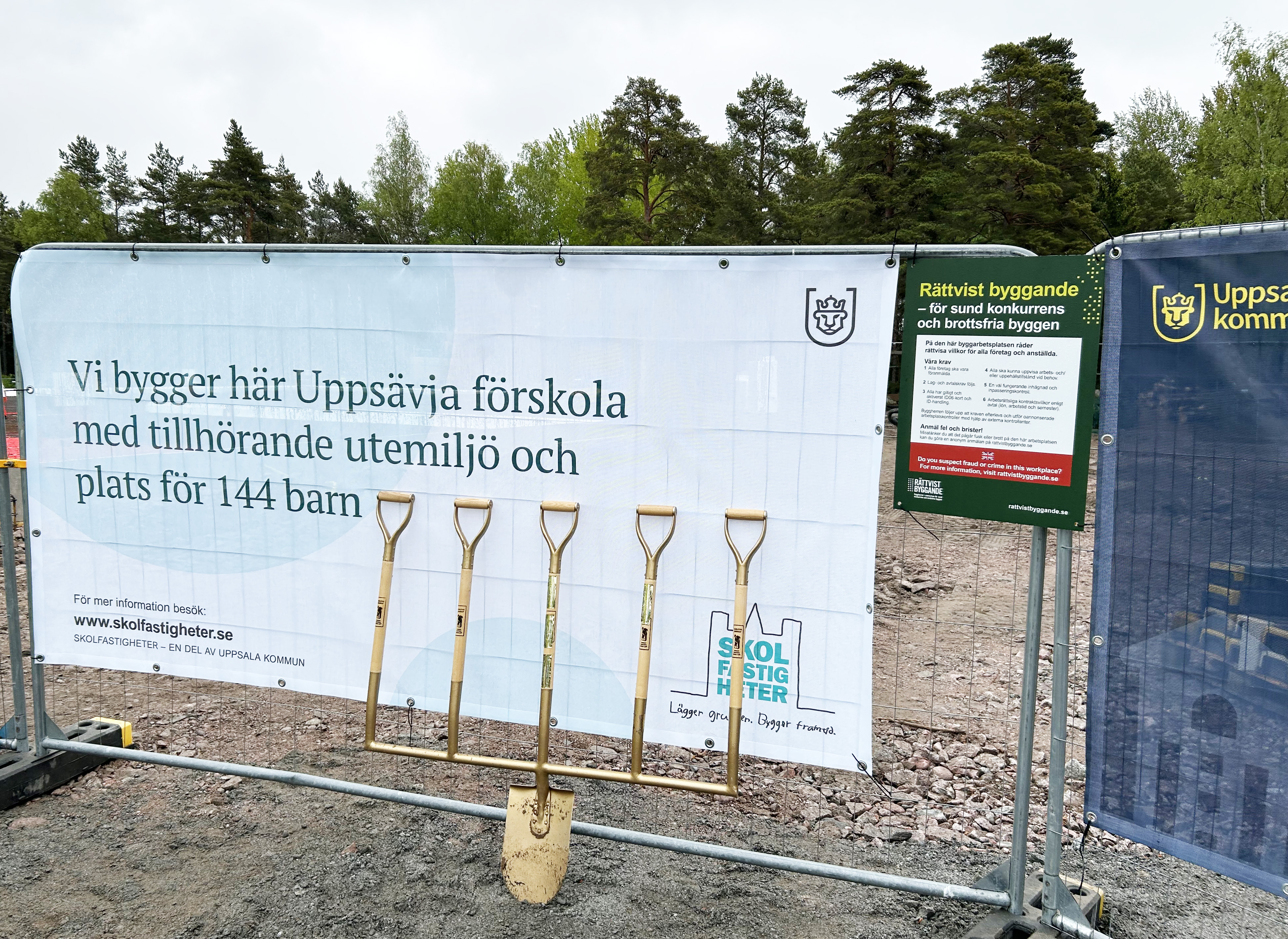Byggvepa med spadar mot stängsel vid en byggplats.