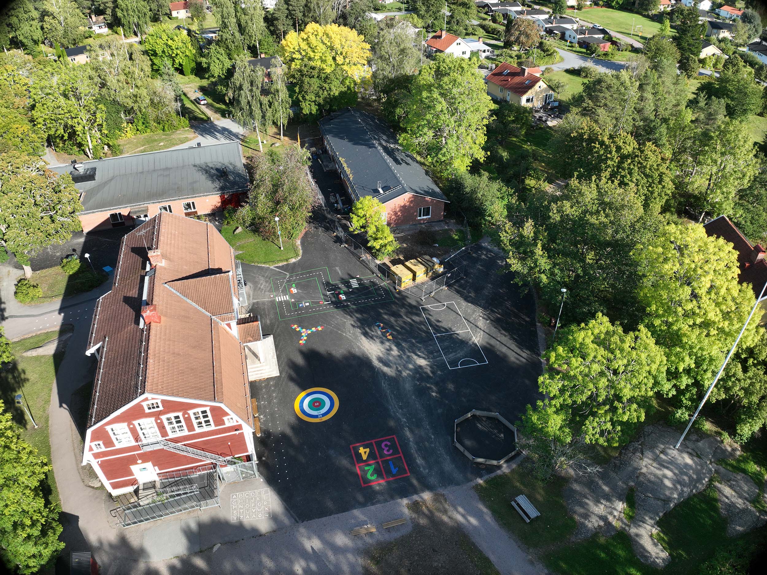 Flygbild över renoverad skola och skolgård med träd, buskar och färgglatt målade asfaltsytor.