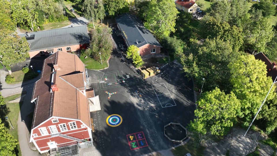 Flygbild över renoverad skola och skolgård med träd, buskar och färgglatt målade asfaltsytor.