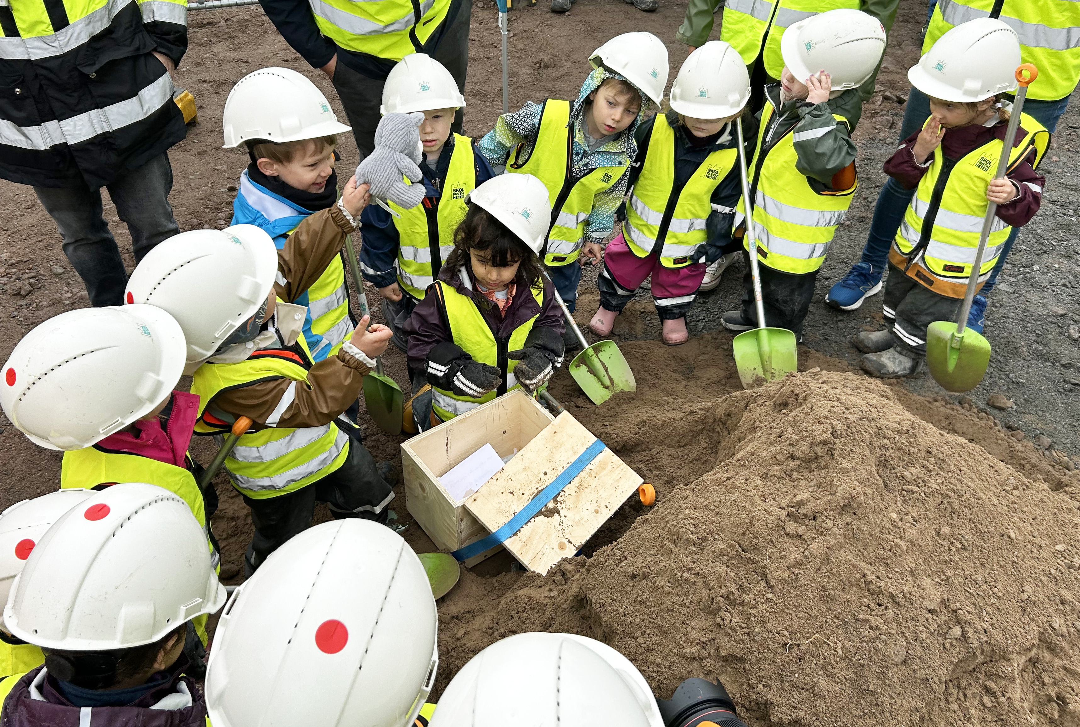 Förskolebarn i gula västar gräver i sandhög på en byggplats.