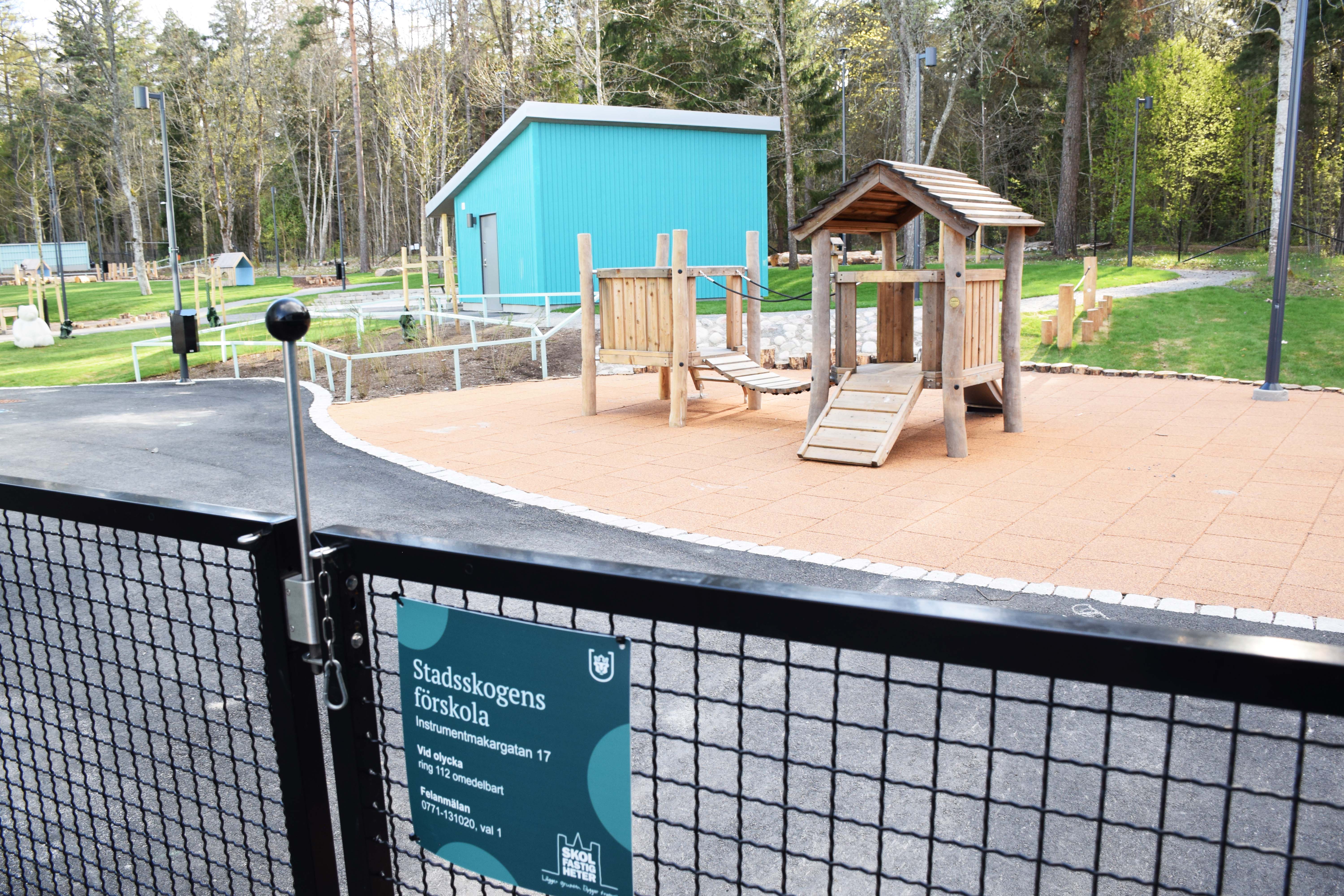 Förskolegård med lekutrustning i trä och skog i bakgrunden.