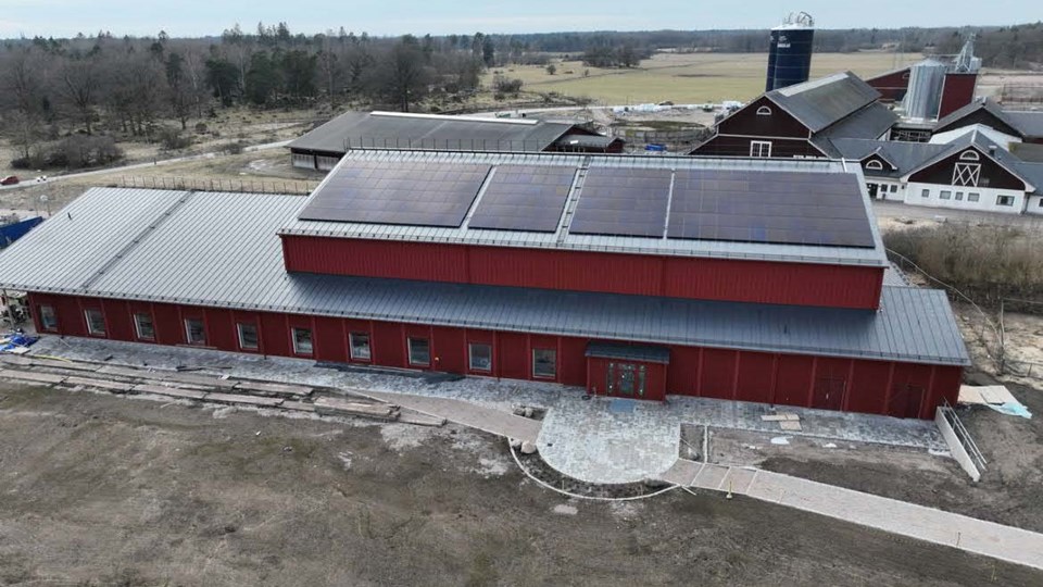 Röd byggnad med solcellsanläggning, sedd från ovan och belägen i lantbruksmiljö.