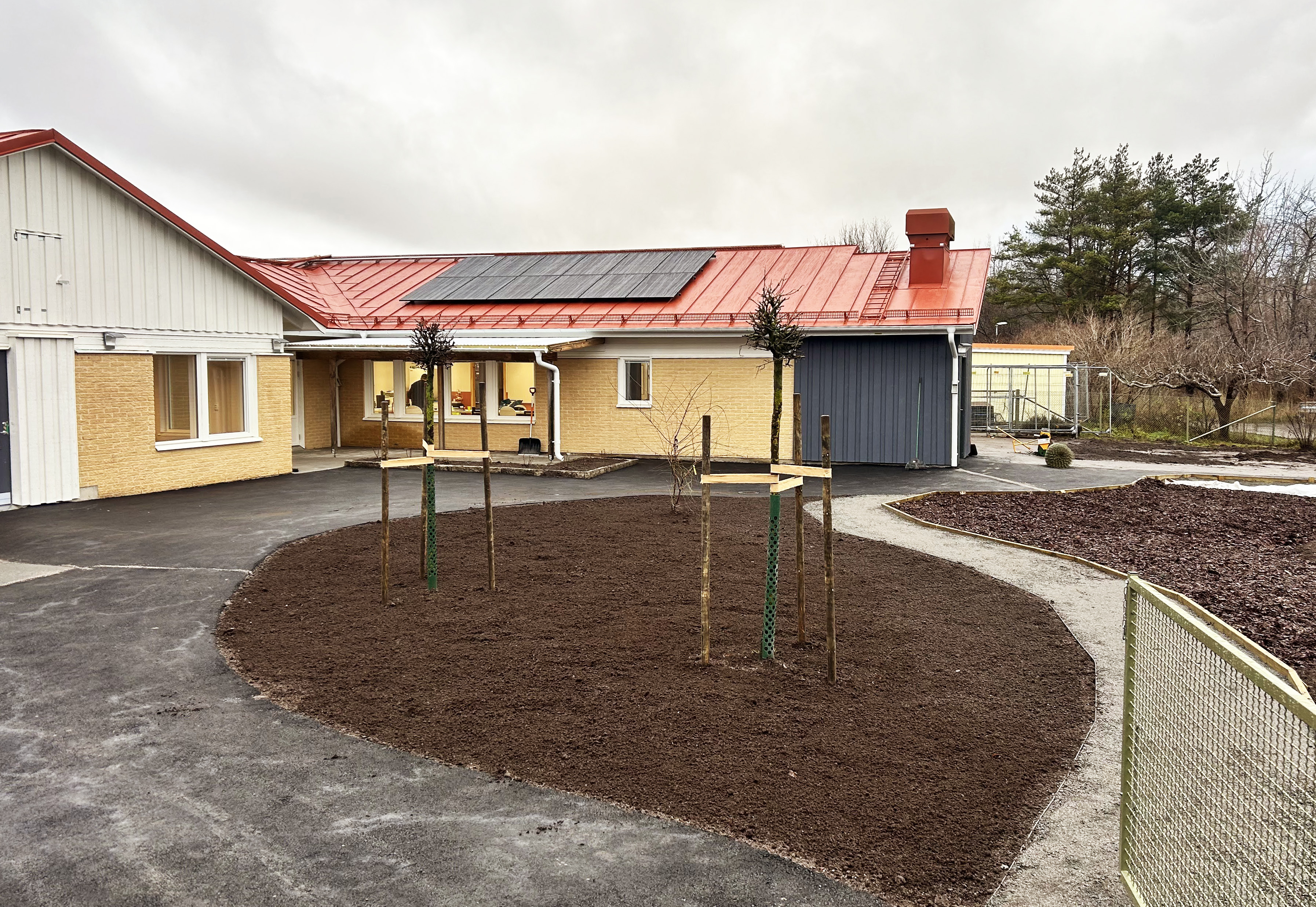 Nyrenoverad förskola i gult tegel med nyplanterat gräs och träd i förgrunden.