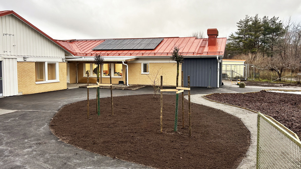Nyrenoverad förskola i gult tegel med nyplanterat gräs och träd i förgrunden.