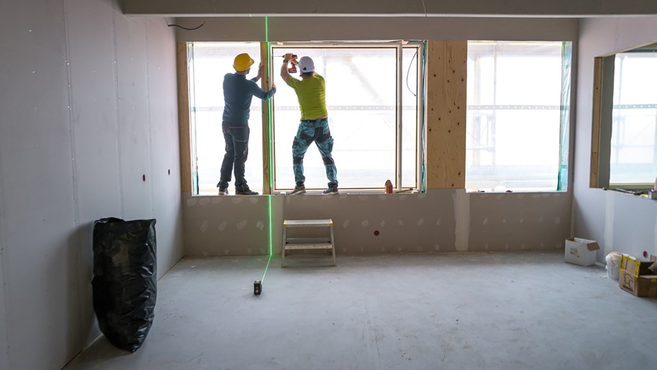 Två byggarbetare monterar tillsammans ett fönster på en byggplats