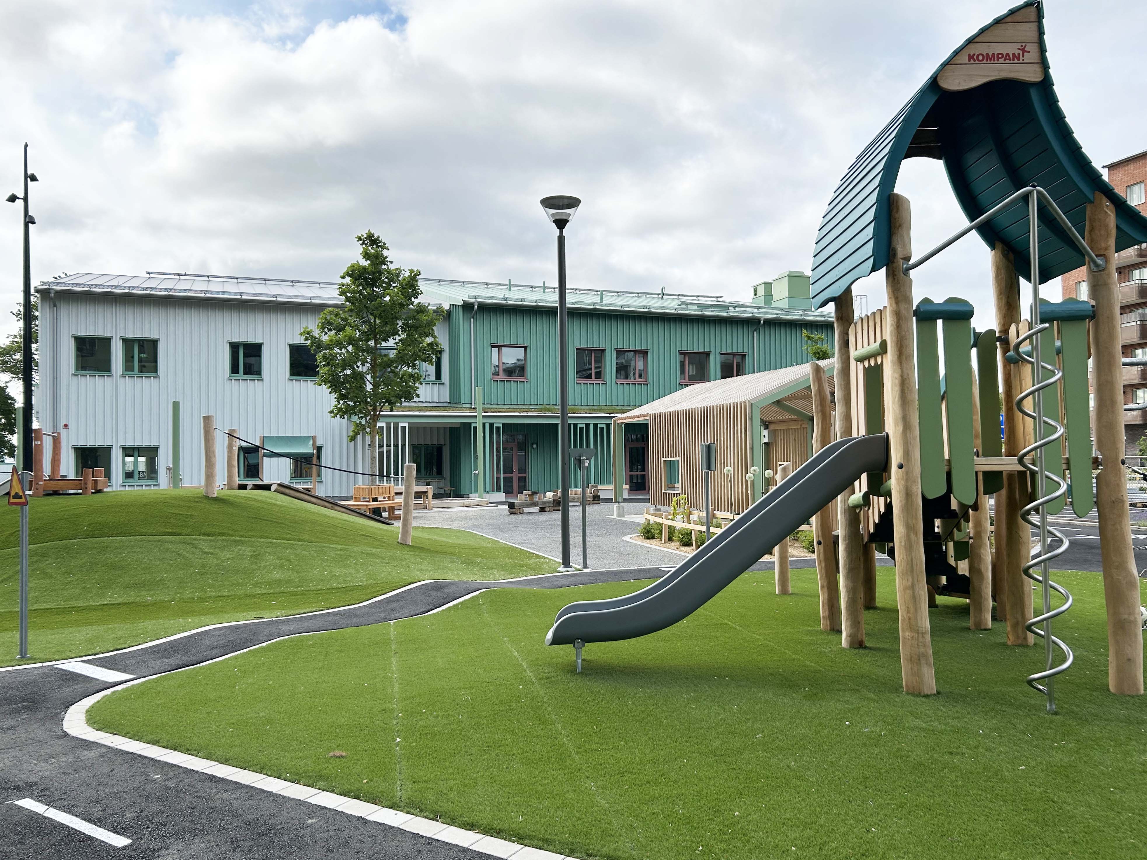 Nybyggd förskola i turkos färg, med lekutrustning av trä i förgrunden.
