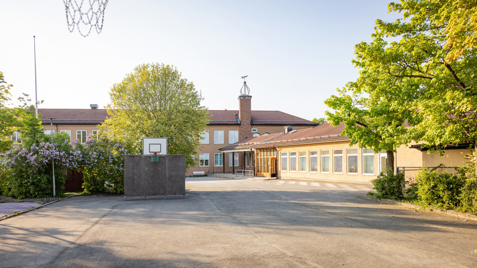 Skolgård med basketkorg och skolbyggnader i bakgrunden