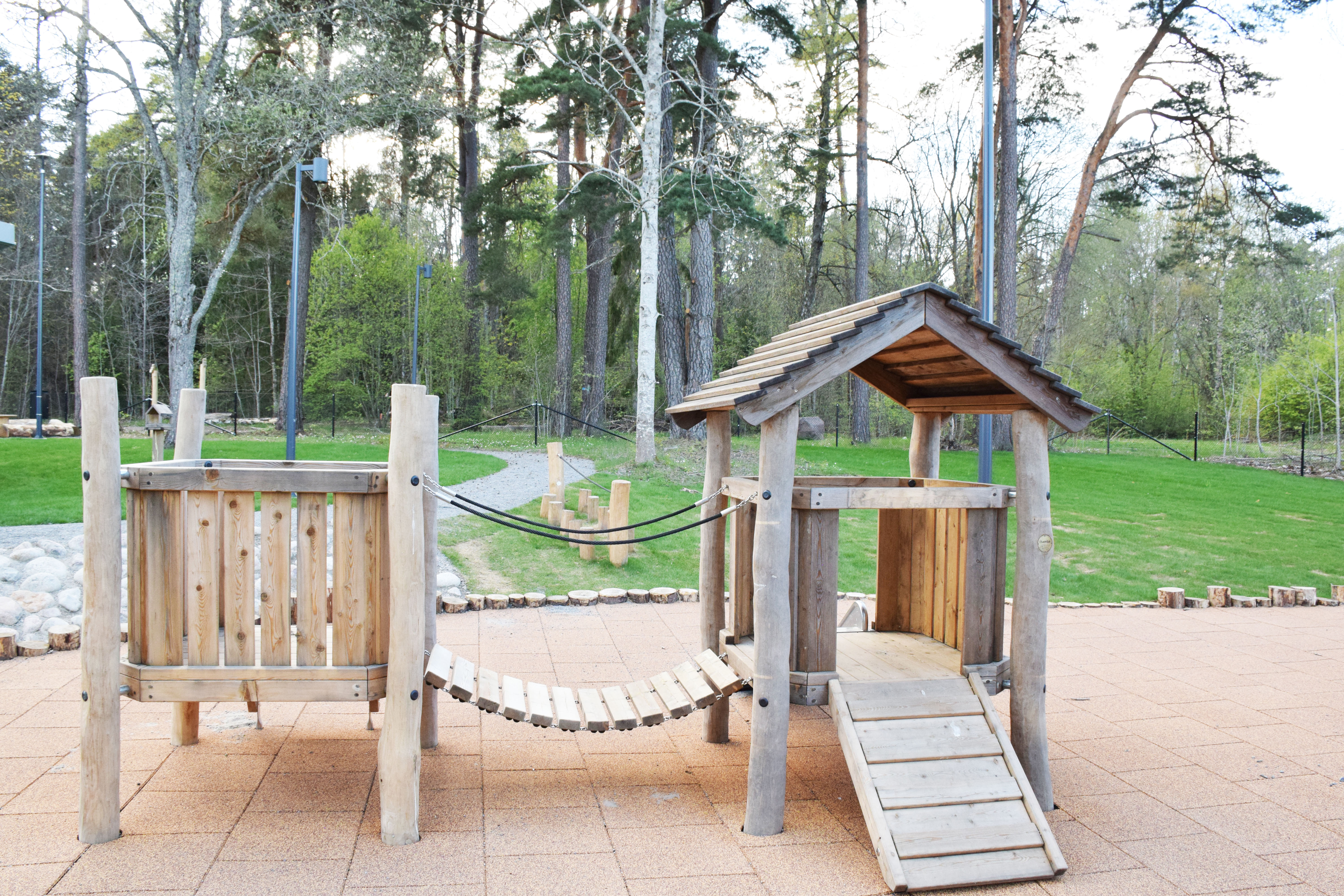 Förskolegård med lekutrustning i trä och skog i bakgrunden