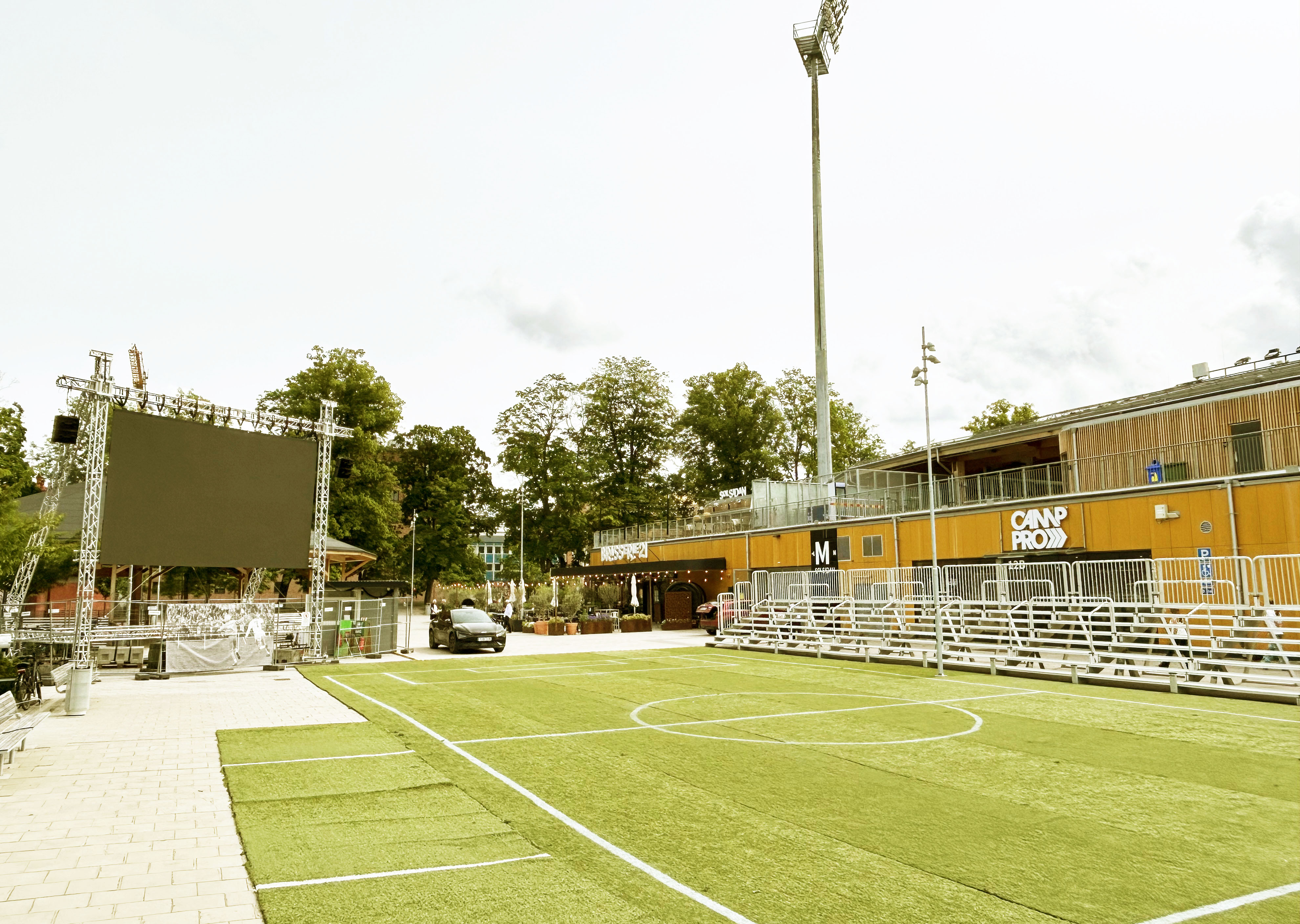 Storbildsskärm med läktare och konstgräsyta framför en arena.
