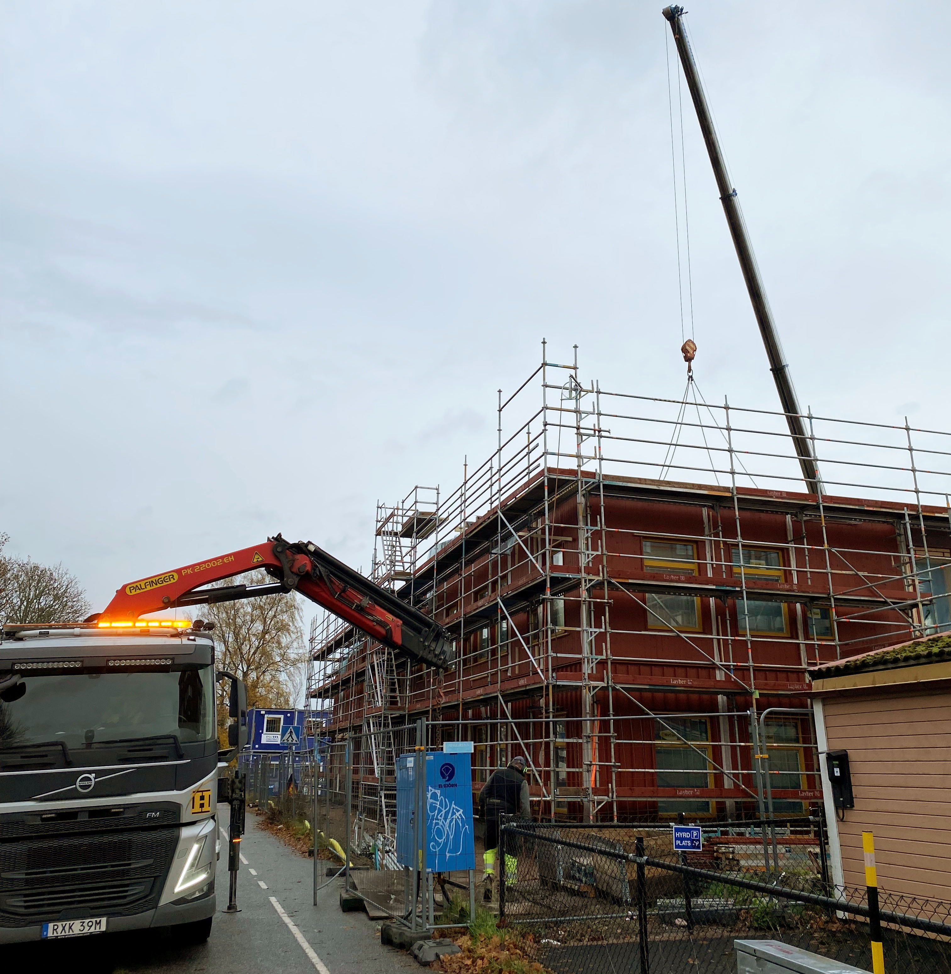 Byggplats där en ny, röd förskola växer fram med parkerat arbetsfordon i förgrunden.