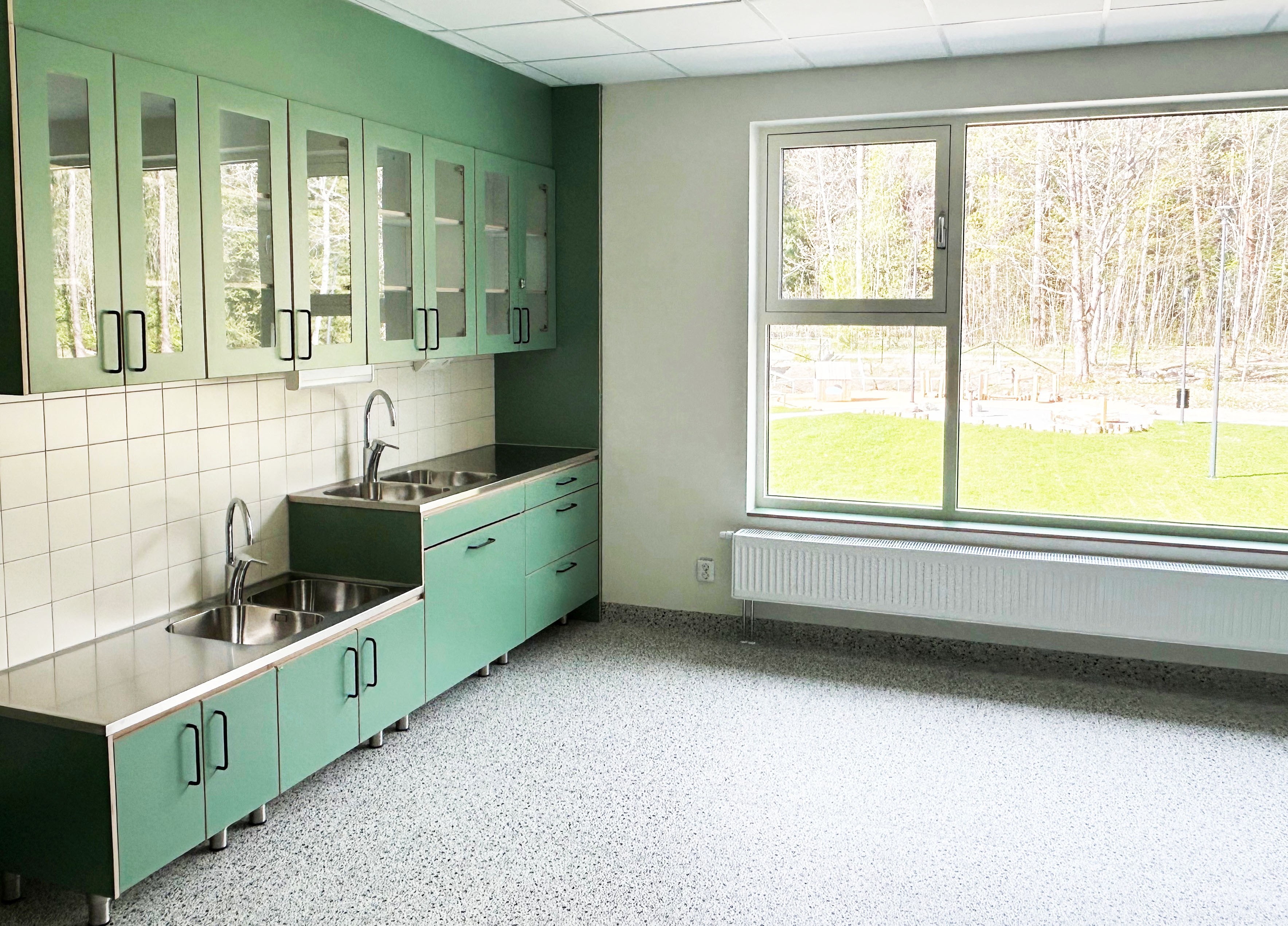 Nybyggd förskola med grönt pentry och stort fönster ut mot gården.