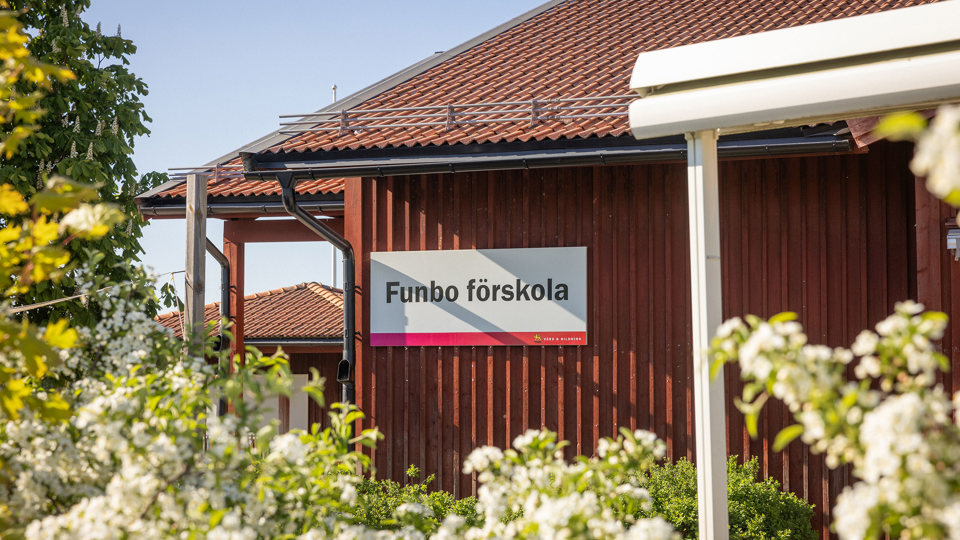 Röd trävägg med förskoleskylt och blommor i förgrunden 