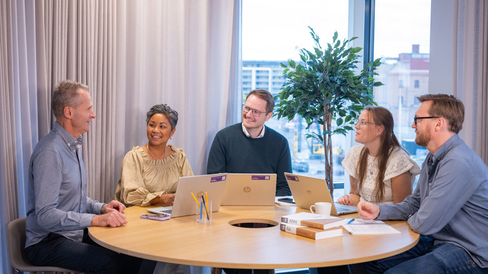 Fem kollegor arbetar med dator vid ett bord