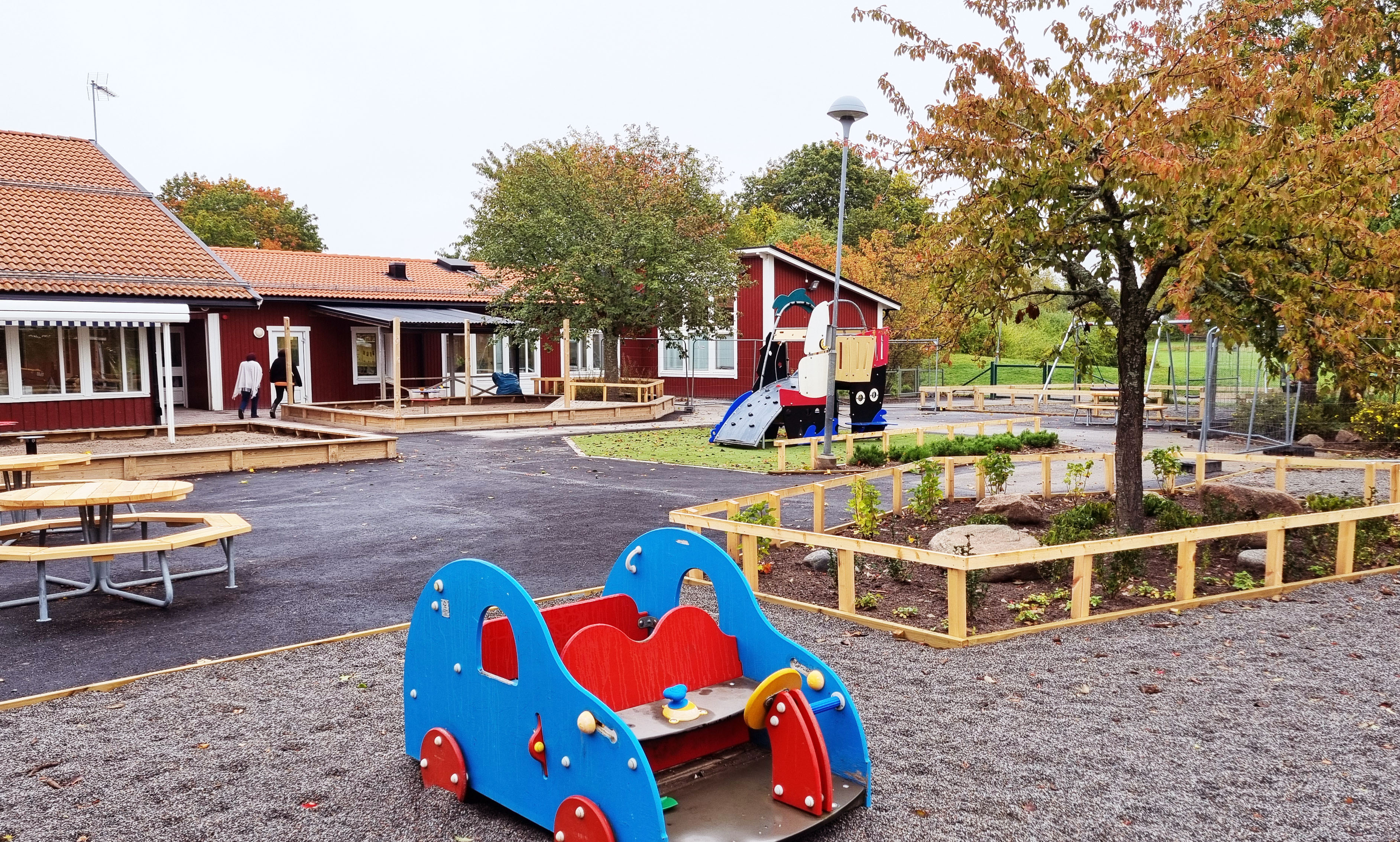 Nyrenoverad gård på en röd förskola med lekutrustning och nya träkonstruktioner.