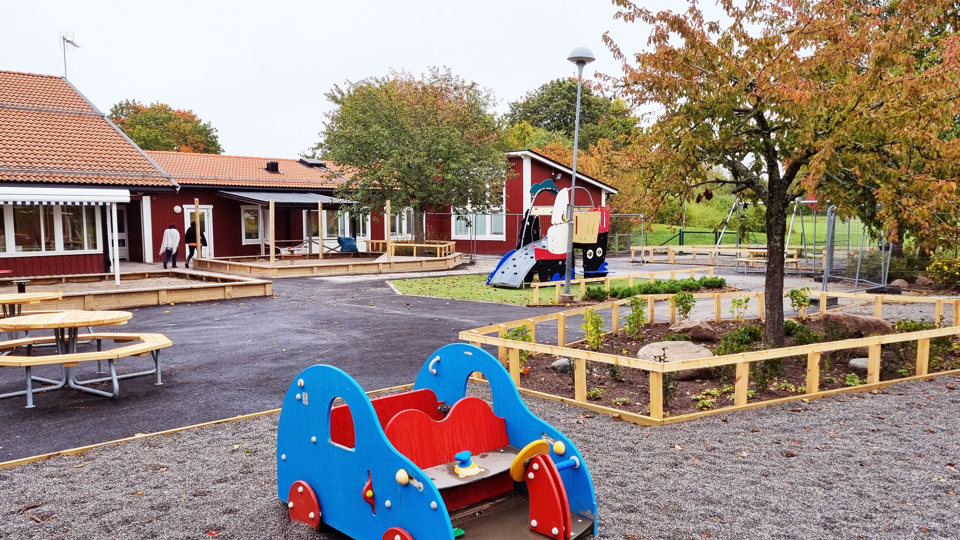 Nyrenoverad gård på en röd förskola med lekutrustning och nya träkonstruktioner.