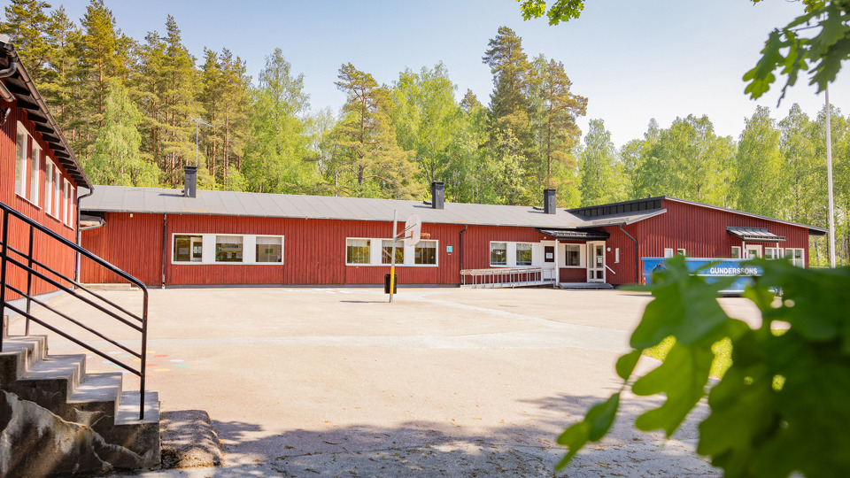 Röd träskola med grusplan i förgrunden och bakomliggande skog.