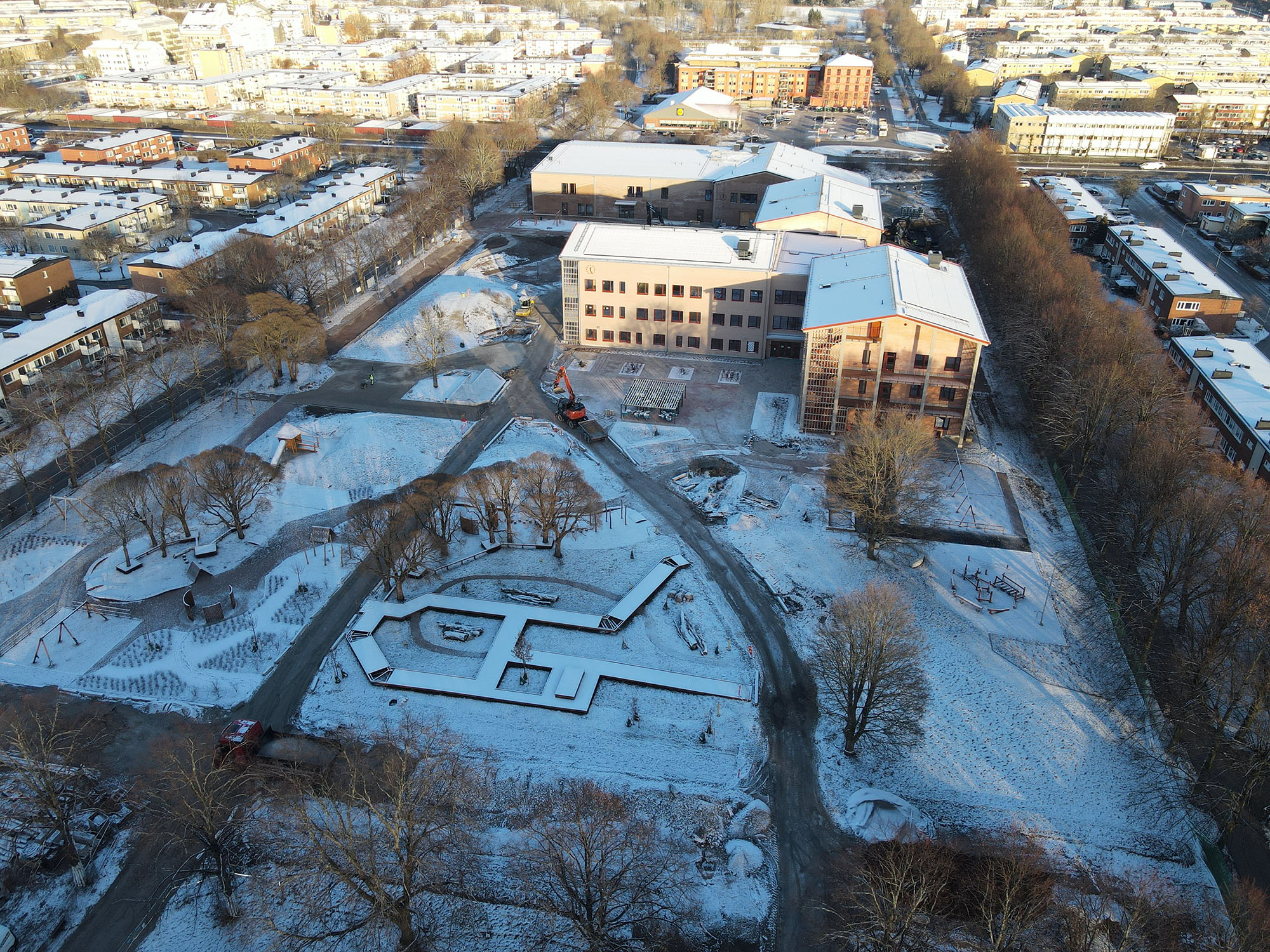 Flygfoto av stor byggplats med flera stora, snötäckta skolbyggnader.