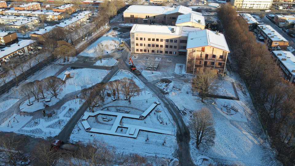 Flygfoto av stor byggplats med flera stora, snötäckta skolbyggnader.