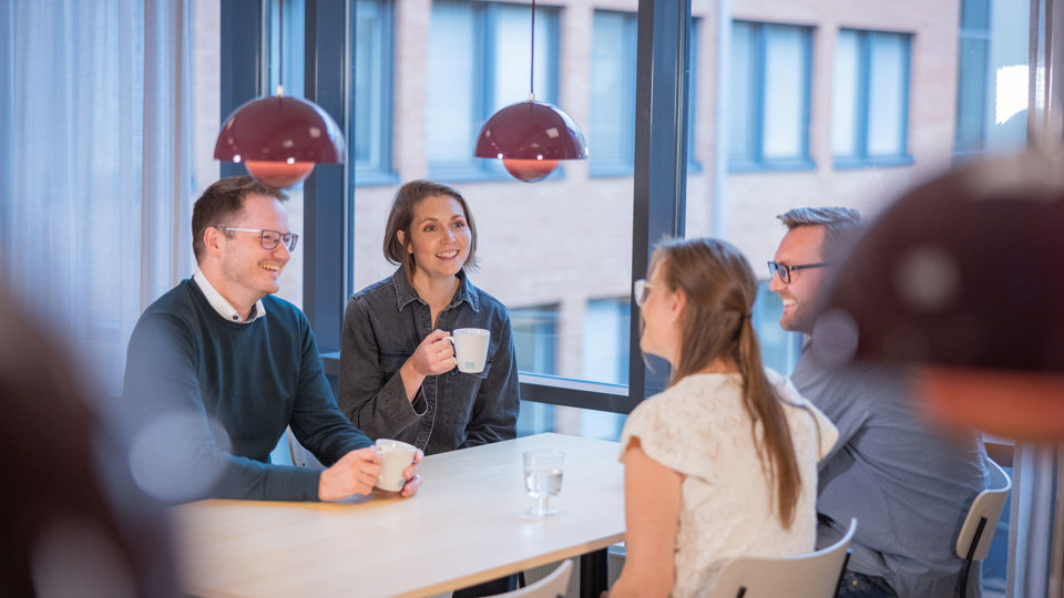 Fyra kollegor som sitter och fikar vid ett köksbord