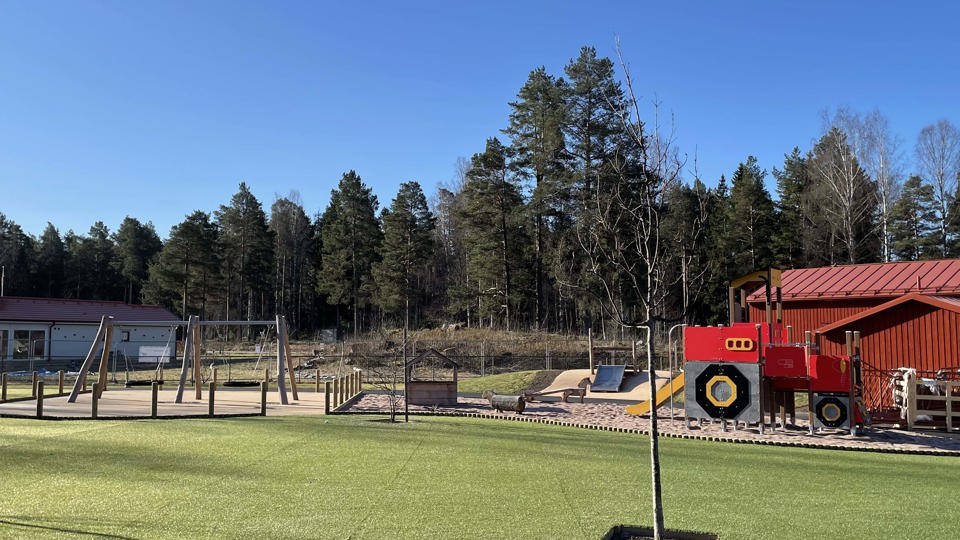 Ny förskolegård  under uppbyggnad med konstgräs och lekställningar i förgrunden.