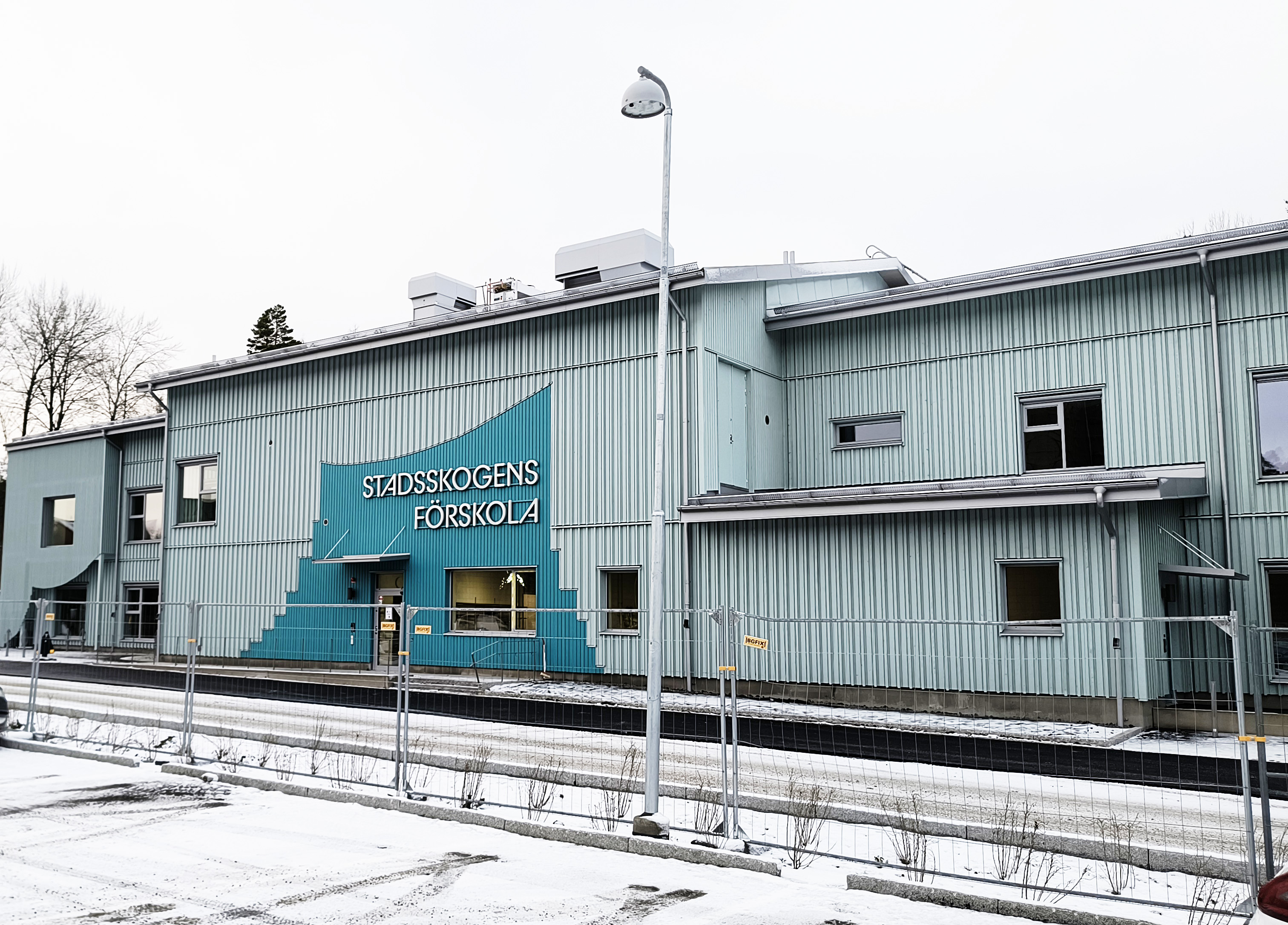 Grön förskola i trä med snötäckt mark i förgrunden.