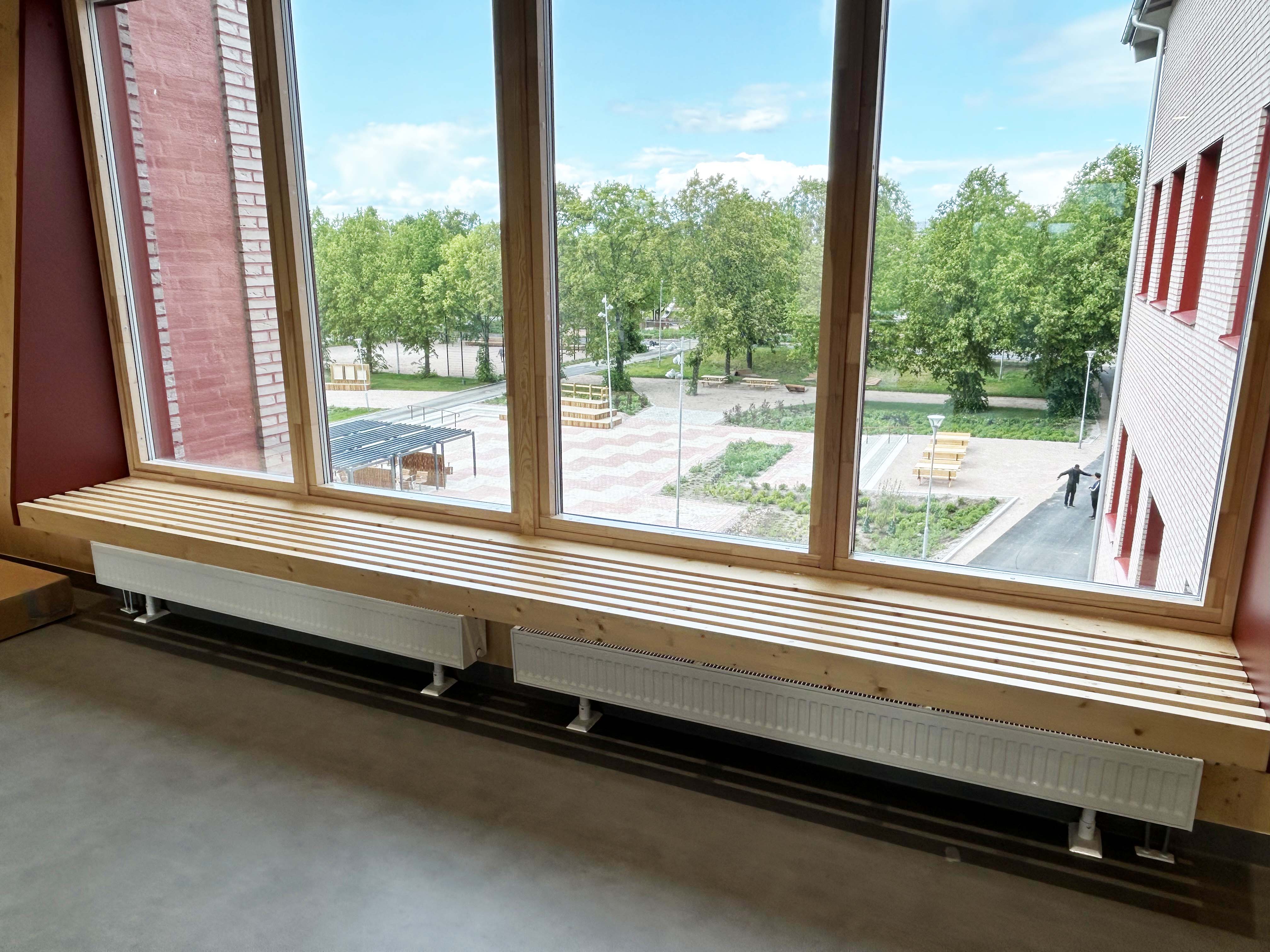 Träbänkar i vid fönster med utsikt mot en nyanlagd skolgård.