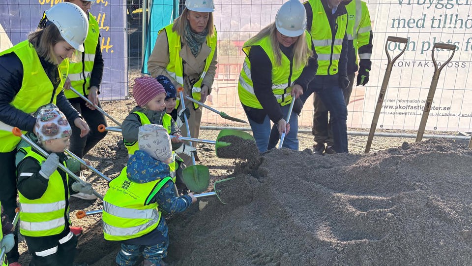 Förskolebarn med gula byggvästar gräver i en grushög på en byggplats.